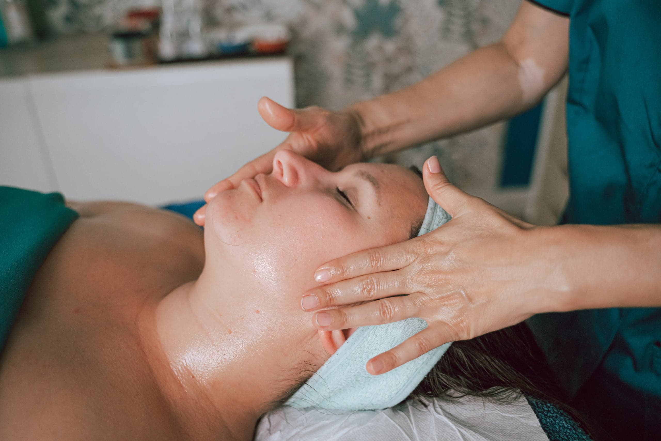 Visage d'une cliente aux yeux fermés, les mains de la praticienne sur la tempe et la mâchoire pendant un massage Kobido, à Vertou